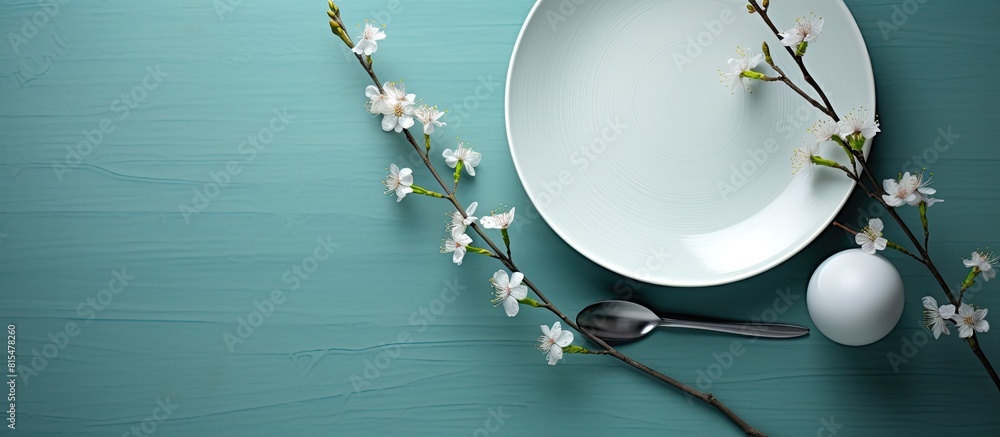 Poster A turquoise table serves as the backdrop for an empty white dish accompanied by a knife and fork A cotton branch adds a touch of elegance Copy space image available for menu or recipe