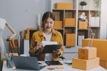 Asian SME business women use laptop computer checking customer order online shipping boxes at home....