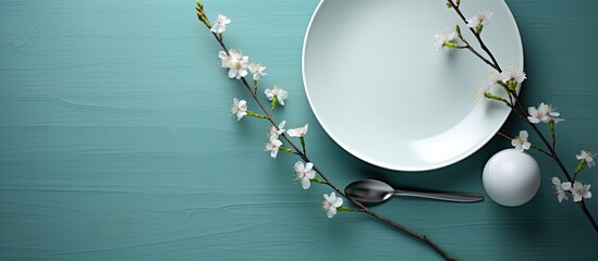 A turquoise table serves as the backdrop for an empty white dish accompanied by a knife and fork A cotton branch adds a touch of elegance Copy space image available for menu or recipe
