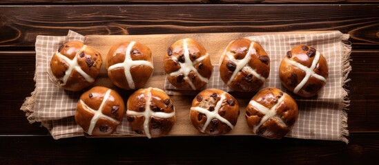 A view from above shows a pack of nine traditional Easter hot cross buns placed on a wooden board over a table cloth illuminated by soft natural light. Creative banner. Copyspace image