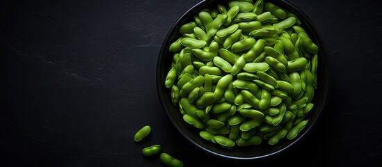 A copy space image of uncooked green broad beans arranged in a bowl captured from a top down perspective on a black kitchen slate tile devoid of any human presence