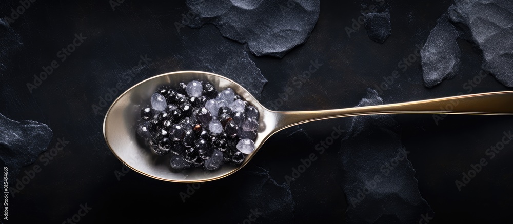 Poster Top view of a silver spoon holding black sturgeon caviar placed on a black slate stone background with enough space for adding text or other images. Creative banner. Copyspace image