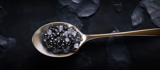 Top view of a silver spoon holding black sturgeon caviar placed on a black slate stone background with enough space for adding text or other images. Creative banner. Copyspace image