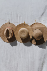Three straw hats hanging on a rope over white cloth with sunlight shadows