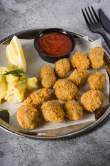 Fried mussels on a metal plate with potato salad on the side. Turkish name: Midye Tava