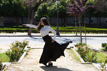 Beautiful woman with long curly hair, dancing flamenco artfully in a park in Seville, Spain....