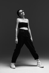 Fashion portrait. A girl in a swimming cap, black top, pants, white sweatshirts and sunglasses poses in the studio.