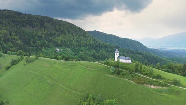 Flying away from Catholic church at the top of the hill, the St. Primus and St. Felician church at Jamnik, Slovenia. Hiking, pilgrimage, travel and tourism concepts. Drone shot, 4K, 60FPS
