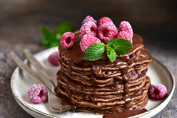 Chocolate banana pancakes with sauce and raspberries.