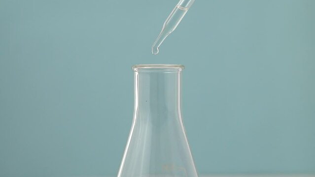 Macro video of dropper & beaker on plain background. Close up of scientific lab equipments on coloured background. Drops of transparent liquid falling from top.