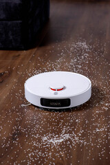 Robot vacuum cleaner vacuums the floor near the sofa. A smart home with automated devices that make...