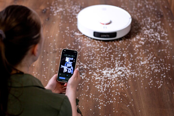 Young woman using smartphone to control smart robot vacuum cleaner