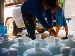 Workers lift drinking water .clear and clean in white plastic gallon into the back of a transport...