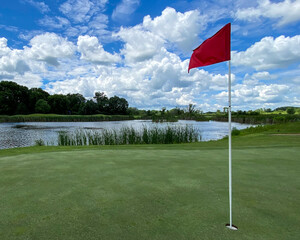 Obraz premium Golf Green with Red Flag Pin Water Hole in Late Spring