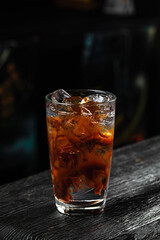 A glass of refreshing espresso tonic cold coffee drink with ice cubes, on wooden table