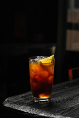 A glass of refreshing espresso tonic cold coffee drink with lemon wedge garnish, on wooden table