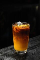 A glass of refreshing iced bumble cold coffee drink with orange juice, on wooden table