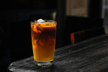 A glass of refreshing iced bumble cold coffee drink with orange juice, on wooden table