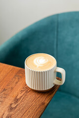 A mug of cappuccino coffee on the edge of wooden table
