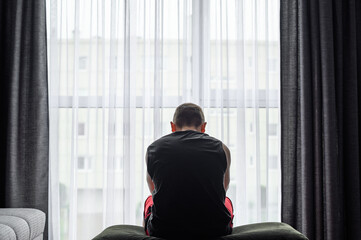 Mężczyzna z depresją siedzi w domu i wygląda załamany przez okno 
