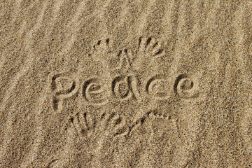 The word PEACE in English. The beautiful word peace is written on the sandy coast. Conceptual inscription on shiny sand and a beautiful seascape background. A word drawn on the beach