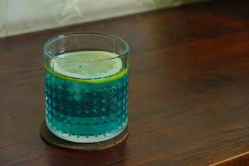 blue tonic water and apple juice with sliced lemon, served with transparent glass on wooden surface