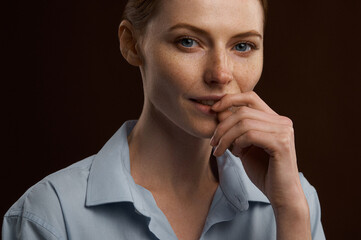 A beautiful red-haired girl with freckles in a shirt posing in the studio on a brown background....