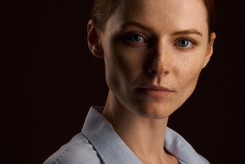 A beautiful red-haired girl with freckles in a shirt posing in the studio on a brown background. grain effect used