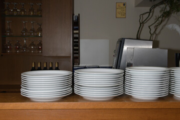 A stack of white clean plates on a wooden counter in a restaurant for the convenience of customers