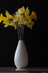 a bouquet of narcissus in a white vase on a black background