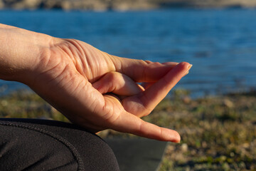 Woman's hand doing a mudra in nature with a lake behind