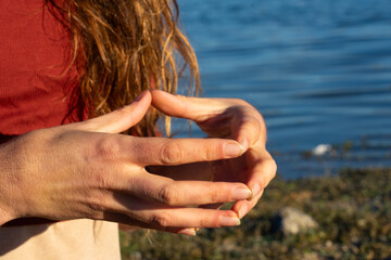 Woman's hands doing the hakini mudra in nature with a lake behind