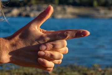 Woman's hands doing kali mudra in nature with a lake behind