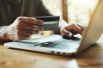 A person holding their credit card, about to make an online shopping order on the laptop computer in front of them.
