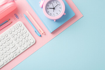 A tidy workstation featuring a white keyboard, pink alarm clock and various stationery items on a...
