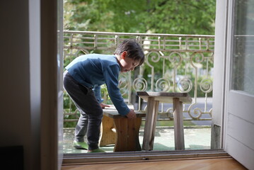 Captured from a lower angle, the boy continues to sit on the wooden bench, gazing downwards. The...