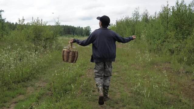 A teenager in a cap and with a basket is walking along the road in the forest for mushrooms.