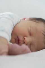 The newborn is asleep on a white blanket, with one arm stretched forward and the face turned...