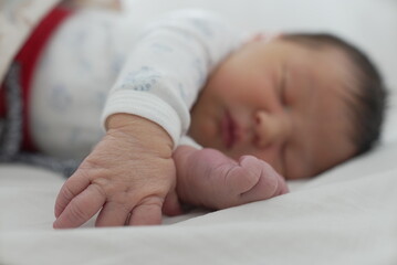 Close-up of a newborn baby sleeping on a white bed, highlighting the small, delicate hand and foot....