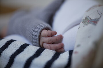 A close-up of a newborn baby's hand resting gently on a striped blanket. The baby is wearing a cozy...