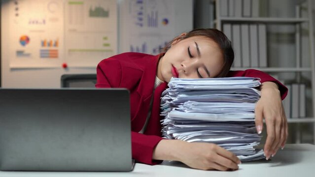 Tired Asian businesswoman Stress from paperwork, headache, sleepiness on piles of documents. Bored from sitting at a desk for a long time and has office syndrome.