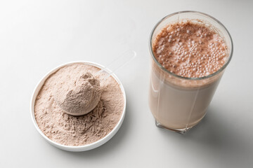 Whey protein powder in a measuring scoop and protein drink cocktail in a glass