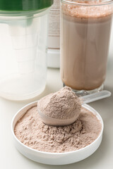 Whey protein powder in a measuring scoop and protein drink cocktail in a glass