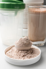 Whey protein powder in a measuring scoop and protein drink cocktail in a glass