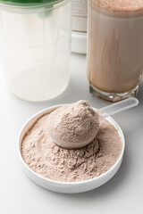 Whey protein powder in a measuring scoop and protein drink cocktail in a glass