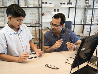 Happy Indian father and cute son choosing eyeglasses in an optics store..