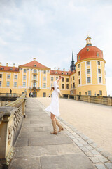 girl in a white dress, beige boots and a beige hat dancing near Moritzburg Castle
