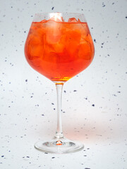 A close-up of a chilled Aperol Spritz filled with ice cubes. The vibrant orange drink stands out against a speckled background.    