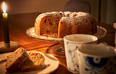 Romantic ambiance with a donut, hot coffee and a burning candle. Cozy setup on wooden table with a doughnut and a mug of warm tea under candle light. Sliced ring shaped cake or paste is ready to eat