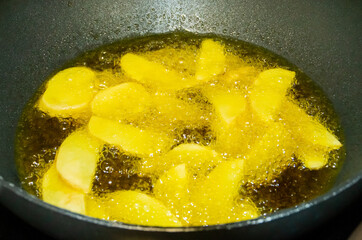 Primer plano de patatas friéndose en aceite caliente. Trozos de patatas rodeadas de burbujas del aceite hirviendo en su proceso de elaboración. French fries.